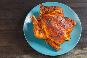 Whole baked chicken carcass with a crust on a platter on a wooden table. save a place.
