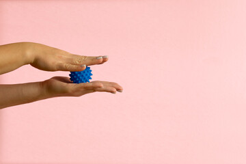 Womans hand with Spiny plastic blue massage ball on pink background
