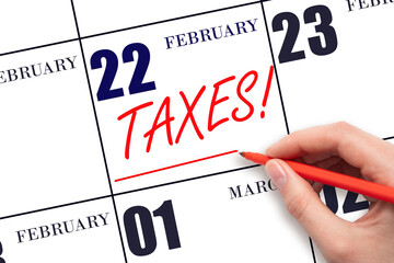 Hand drawing red line and writing the text Taxes on calendar date February 22. Remind date of tax payment