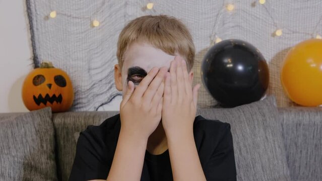 The boy smears makeup on his face with his hands after the celebration of Halloween. Looking at the camera