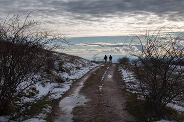 A distant couple on a mountain road, with snow at the sides