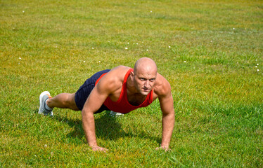 bald male athlete doing push-ups on the green lawn at the stadium. outdoor training. active...