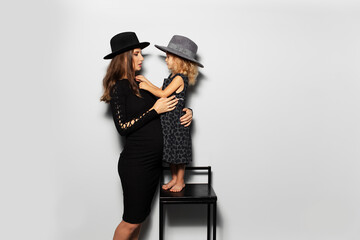 Studio portrait of pregnant smiling woman and child girl looking each ever, wearing hats on white...