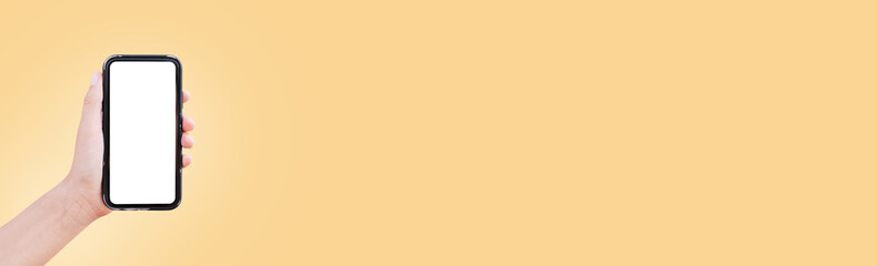 Close-up of male hand holding smartphone with blank on screen on background of pastel yellow color...