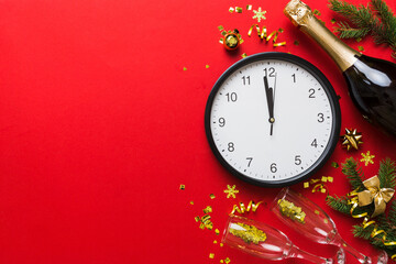 New year celebration concept with a bottle of champagne and two glasses toasting. Christmas gift box, alarm clock and fir tree branch on colored table. Top view Copy space