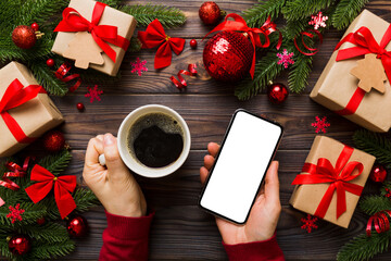 Above view of female hand holding smart phone with hot cup of coffee. Christmas decoration on colored background