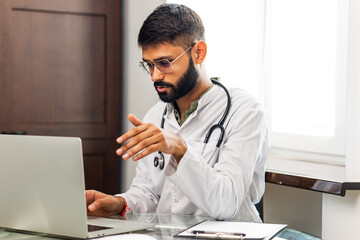 Portrait of indian man doctor talking to online patient on laptop online consultation