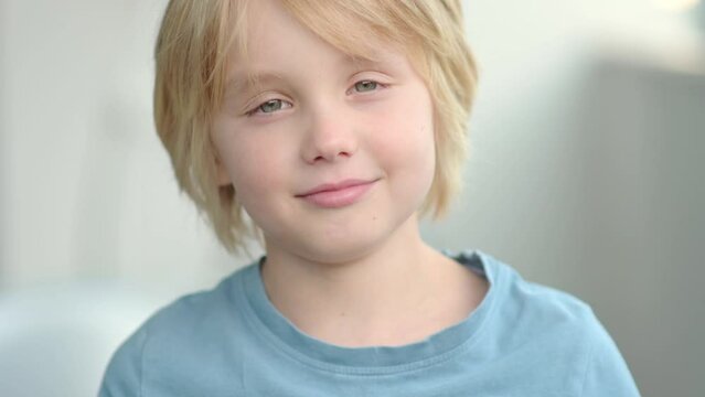 Slow motion close-up portrait of happy school-age child. Cute boy with blond hair emotionally laughs and looks at you. Real emotions of kids. Beautiful european child smiles and rejoices