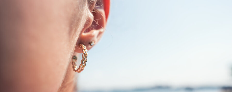Golden earring hanging in ear of young woman with tan skin against blue sky closeup