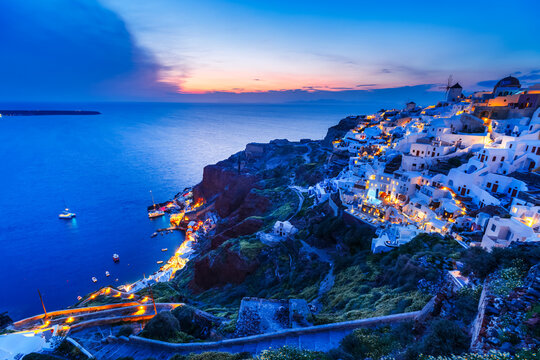 Picturesque view of island Santorini in Greece during twilights. Urbanistic landscape of Oia village in blue tones at Aegean sea and dramatic sky background. Cyclades islands archipelago.