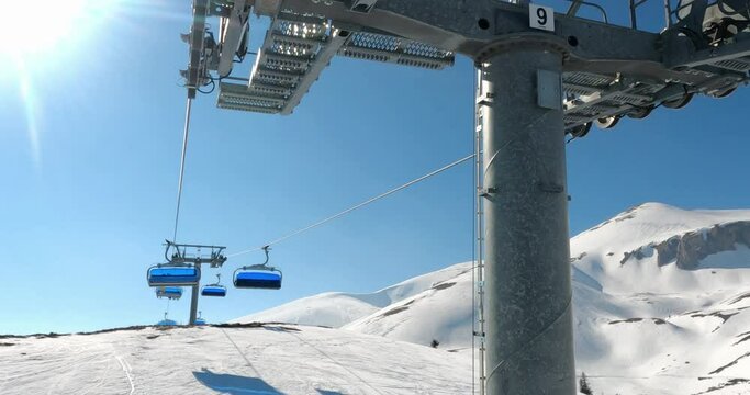 POV from chair ski lift with skiers over blue sky in sunny day with skier ski down the track