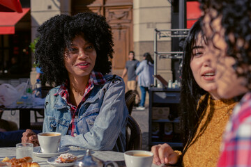 young Haitian Afro woman chatting with her friends at an outdoor cafe in autumn