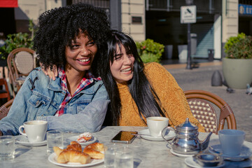 Fototapeta na wymiar young latina and haitian afro woman laughing together embracing in an outdoor cafe in autumn