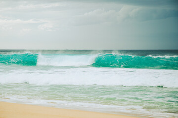 Turqouise wave breaking on sandy beach