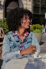 young haitian afro women laughing while drinking coffee at an outdoor cafe in autumn. vertical photo