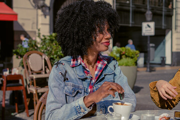 young haitian afro woman sugaring a coffee in an outdoor cafe in autumn