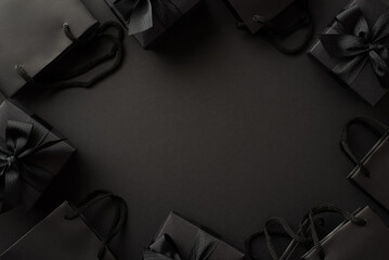 Black friday concept. Top view photo of black gift boxes with ribbon bows and paper bags on isolated black background with copyspace in the middle