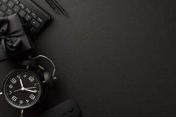Black friday concept. Top view photo of black alarm clock giftbox with ribbon bow pencils computer mouse and keyboard on isolated black background with empty space