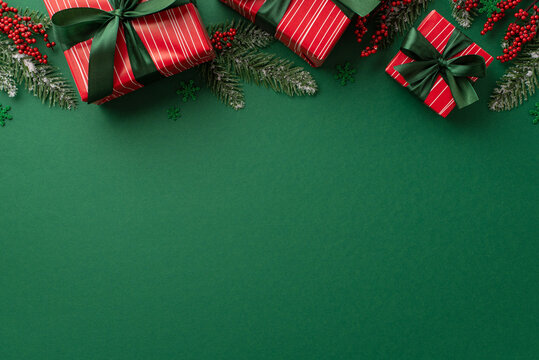 Christmas concept. Top view photo of red present boxes with green ribbon bows mistletoe berries pine branches in hoarfrost and confetti on isolated green background with copyspace