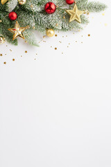 New Year concept. Top view vertical photo of pine branch in snow decorated with red baubles gold star ornaments and confetti on isolated white background with empty space