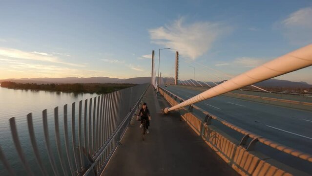 Woman Bike riding on a Bicycle Path over Golden Ears Bridge over the Fraser River. Sunset Sky. Pitt Meadows, Langley, Greater Vancouver, British Columbia, Canada. High quality 4k footage