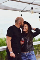 Portrait of happy    smiling  Couple  drinking rose Wine  in a beach bar  against sea during  the winter .Happy Bearded man  kissing and hugging  Brunette woman  in leather jacket and hat on a beach