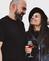 Portrait of happy    smiling  Couple  drinking rose Wine  in a beach bar  against sea during  the winter .Happy Bearded man  kissing and hugging  Brunette woman  in leather jacket and hat on a beach