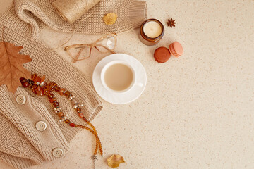 Obraz na płótnie Canvas Feminine trendy outfit - sweater, glasess and brown gemstone jewellery. Autumn aesthetic coffee time among candle, fall leaves, macaroons. Pastel background