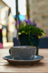 coffee cup on wooden table outdoors with blurred out plant pot in background