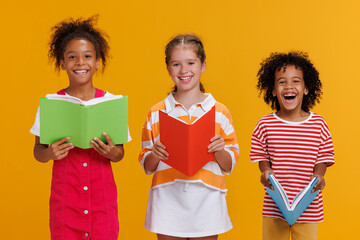 Group of cheerful happy multinational children with books on  yellow background - Powered by Adobe