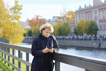 Fototapeta premium Lifestyle portrait of a young man using a smart phone outdoors. man relaxing in autumn park