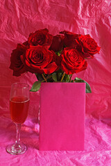 Valentine or any celebratory Red Roses with pink Champagne in flute with pink envelope for copy space and pink background. 