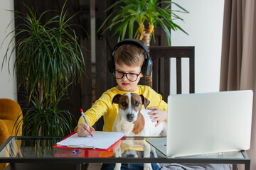 schoolboy in headphones with a dog have a lessons via computer at home