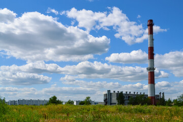 Fototapeta na wymiar Tall striped red and white chimney of a boiler house against the background of white clouds in the blue sky