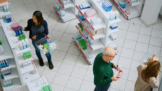 Diverse Clients Waiting In Line To Pay For Medication At Pharmacy Shop Counter, Having Prescription Medicine And Needing Supplements. People Buying Pharmaceutics And Medicaments.