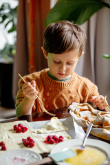 Little boy in sweater cooking cookies at table at home