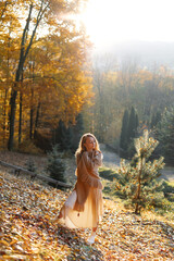 Playful and beautiful young woman in a brown poncho at sunset in the autumn forest.