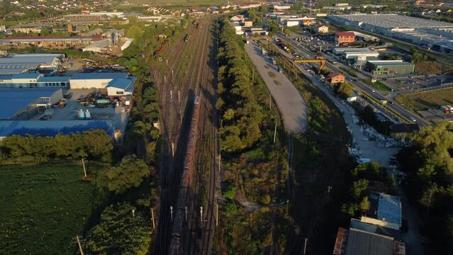 Drone flight in an industrial area. A freight train loaded with wood moves forward, and on the road near the industrial area many vehicles pass.