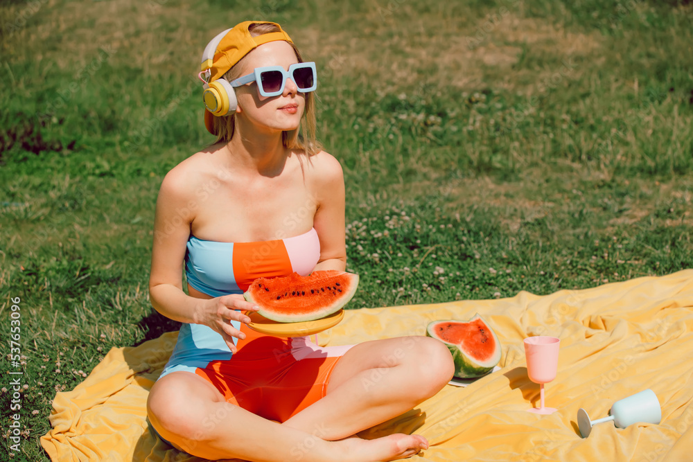 Sticker Stylish woman in headphones eats watermelon in outdoor in summer