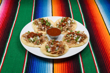 A plate of delicious carnitas tacos with a side of  red salsa.