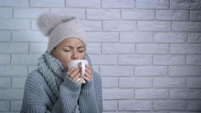 Trying to get warm with hot coffee. A woman in winter cap try to get warm with a hot bevarage in room. A concept of heating crisis in Europe.