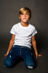 Portrait of a little blond haired boy sitting on his knees in ripped jeans and a t-shirt