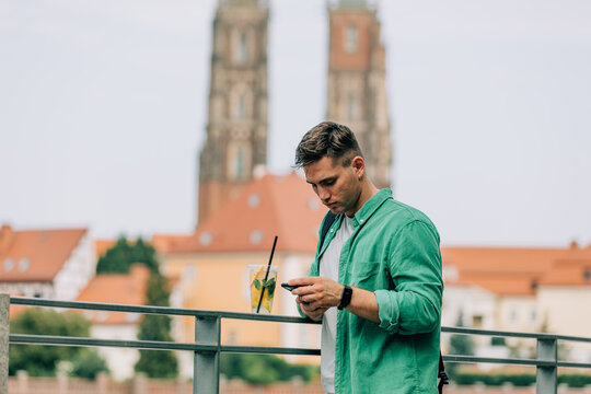 Stylish man in green shirt using mobile phone on near river on city street of Wroclaw, Poland