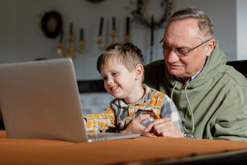 Fototapeta na wymiar Little boy and grandfather using laptop computer at home