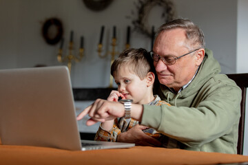 Little boy and grandfather using laptop computer at home