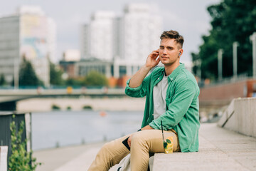 Stylish guy with earphones listen music and sit on city street in Wroclaw, Poland