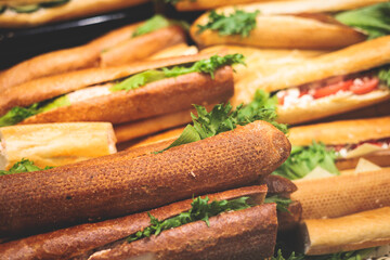 Beautifully decorated catering banquet table on event with different food snacks and appetizers setting with bagel and sandwiches, triange, baguette club submarine sandwich, on a wooden plate