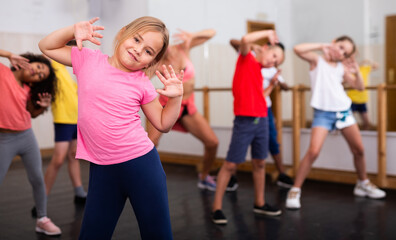 Fototapeta na wymiar Portrait of emotional girl doing dance workout during group class in studio