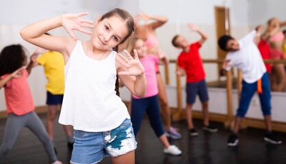 Sporty ten years old girl training movements of vigorous dance during group class in dance school..