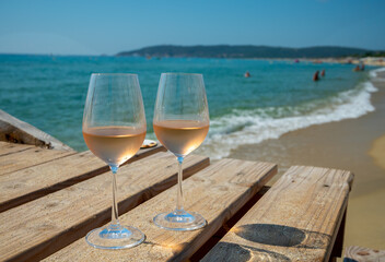 Glasses of cold rose wine from Provence served outdoor on wooden yacht pier with view on blue water and white sandy beach Plage de Pampelonne near Saint-Tropez, France